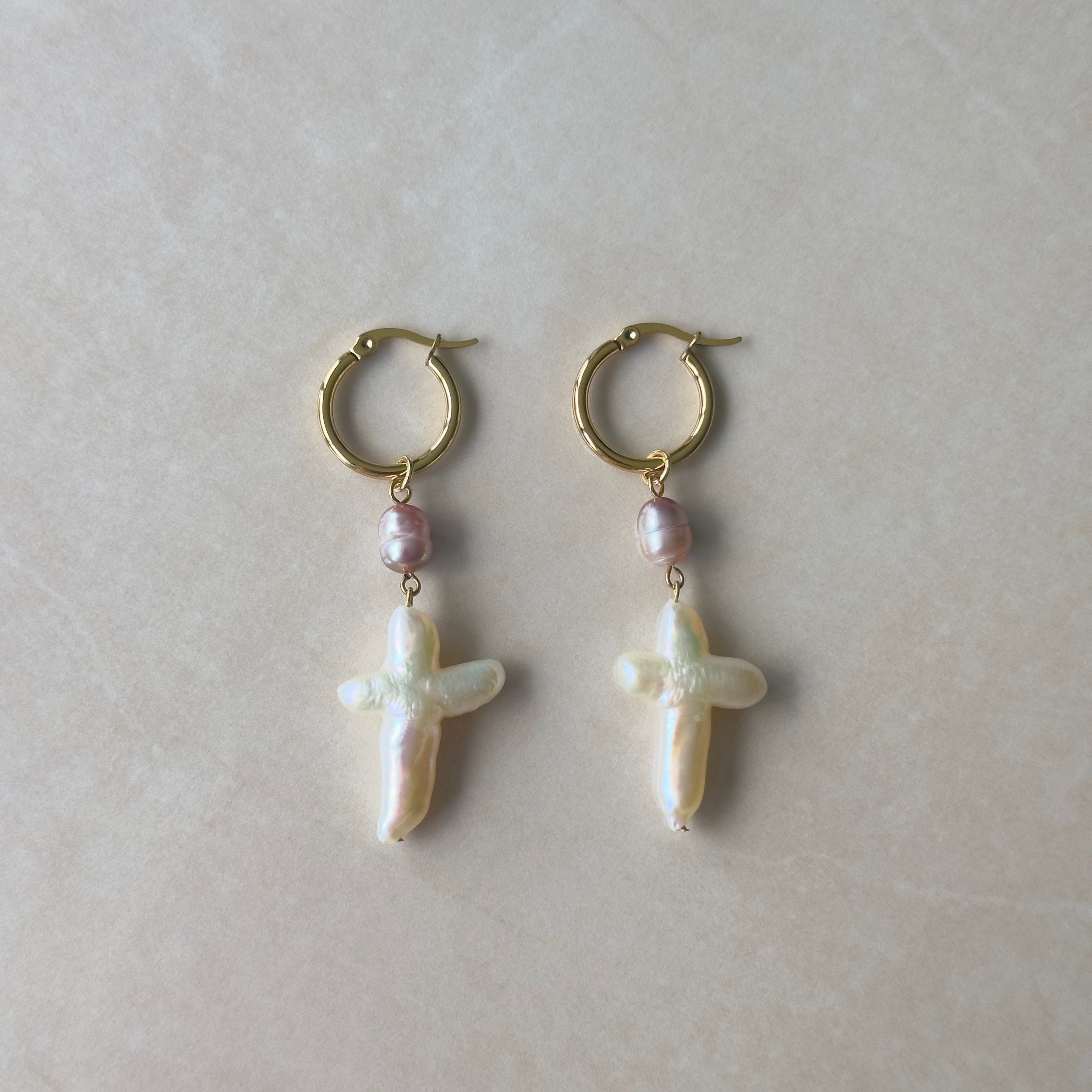 Pair of hoop earrings with cross-shaped pearls on a light background