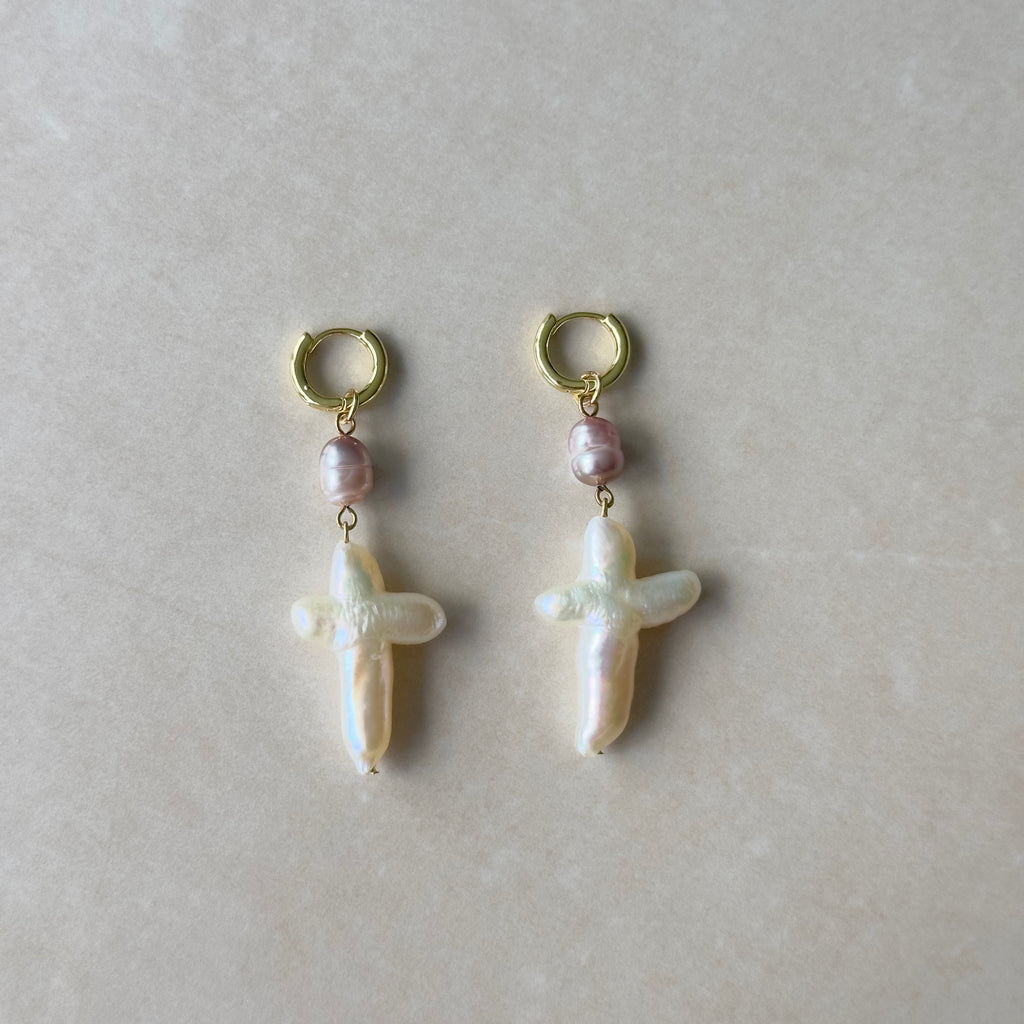 Pair of pearl earrings with gold hooks on a light gray background