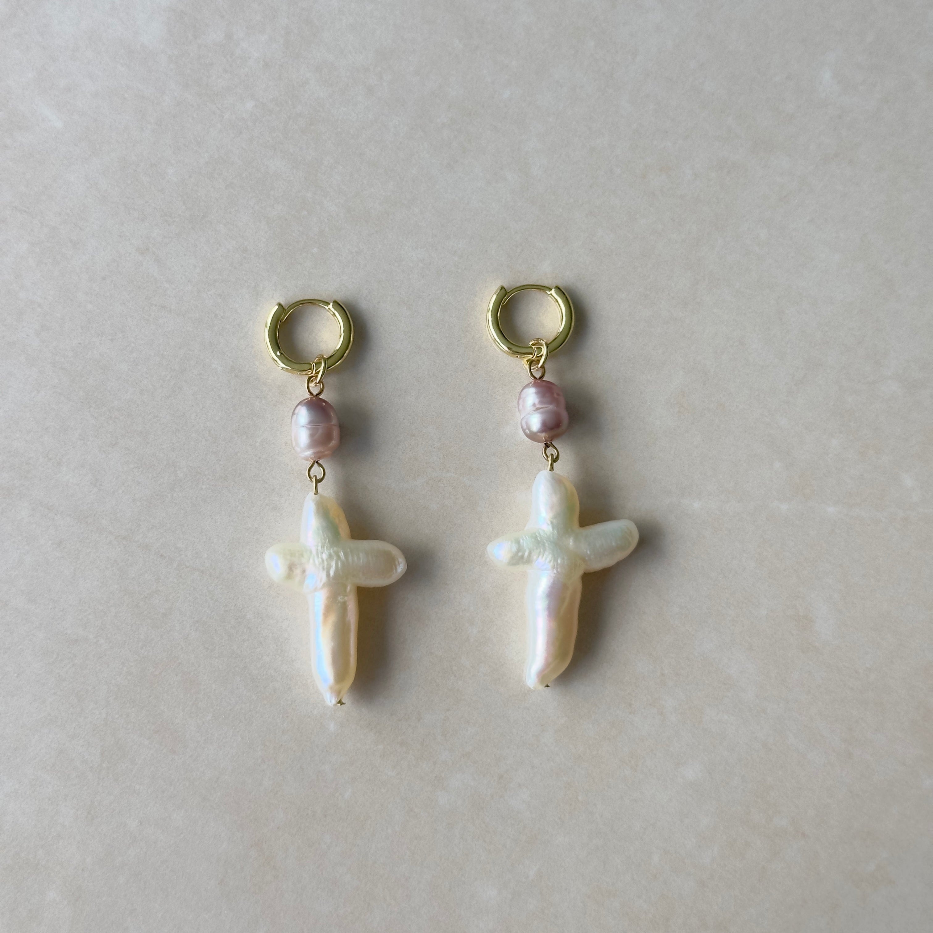 Pair of pearl earrings with gold hooks on a light gray background